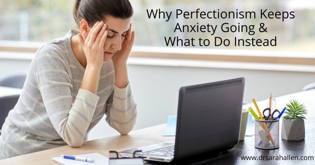 Woman sitting at desk feeling anxious and overwhelmed by perfectionism